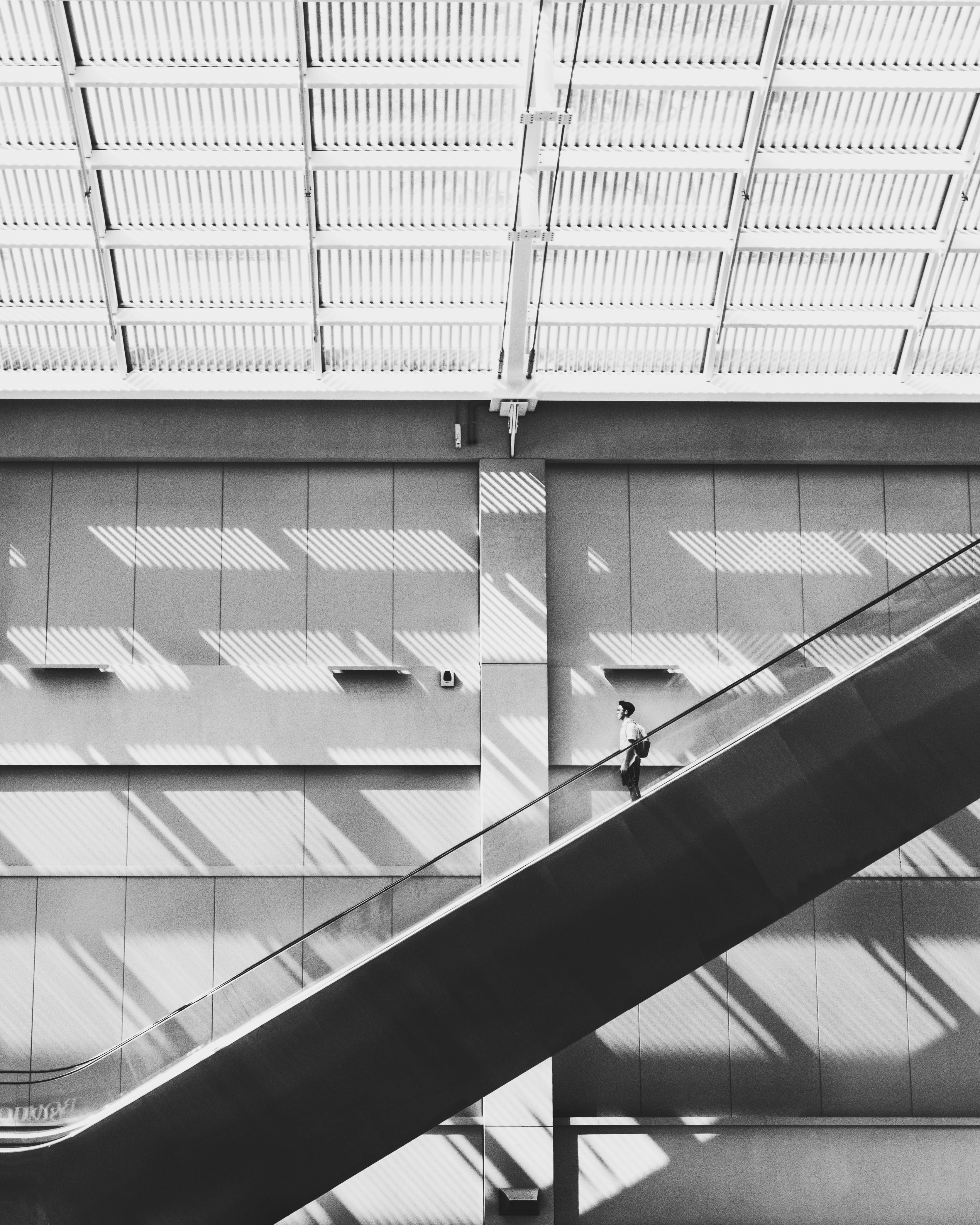 grayscale photo of man standing on escalator